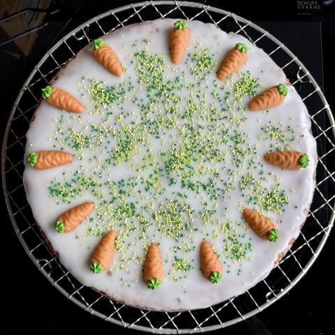 Kuchen mit Zuckerglasur und Marzipanmöhren und grün-gelben Zuckerkügelchen.