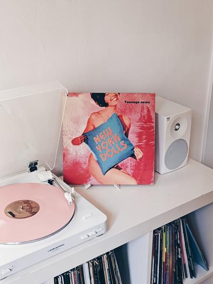 Tocadiscos blanco con un disco de vinilo rosa. Al lado la portada de un disco de los New York Dolls