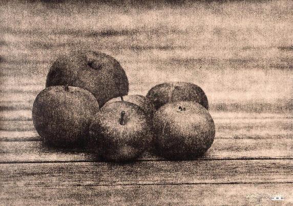 Six apples on a wooden table seen in a monochrome photographic print, processed as lith-print.