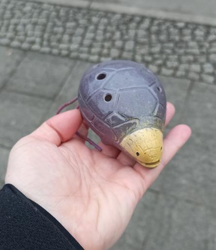 Photo of my hand holding an ocarina that is shaped as a turtle. The head is yellow and the body/shell is greyish purple.