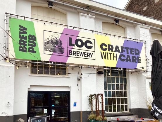 The white front facade of the LOC Brewery brewpub, with a colourful banner with “LOC Brewery, crafted with care” on it
