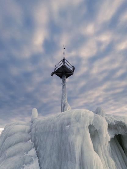 An upwards-looking shot of a lighthouse light with the stairs access to it covered in ice.