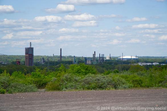A view from a hill to the distance in the direction of the City Gelsenkirchen. You can see the Nordsternpark with the winding tower and Nordstern Tower on the left and the Veltins Arena on the right.