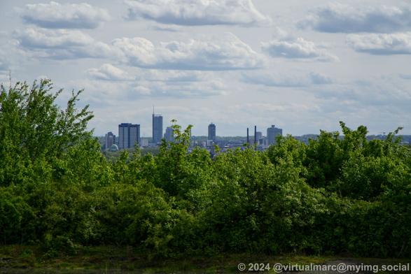 A view from a hill to the distance in the direction of the City Essen where you can see the skyline of the City, including the city hall and the RWE Tower.