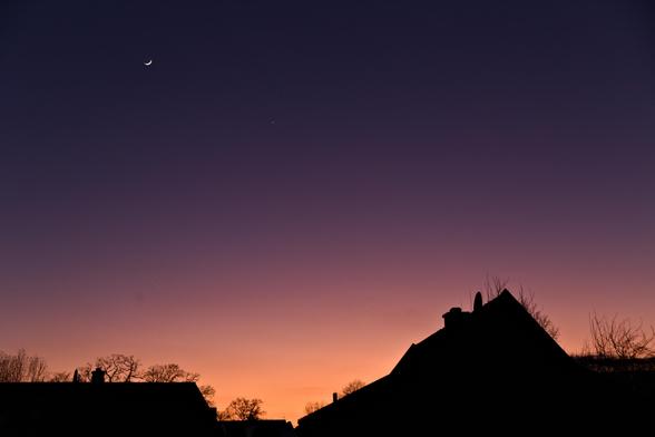 Picture of the evening twilight sky with the Moon and Venus. The sky is strikingly orange and purple.