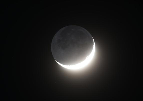 Die überbelichtete zunehmende Mondsichel am dunklen Nachthimmel, die dunkle Seite des Mondes wird als aschfahles Mondlicht sichtbar