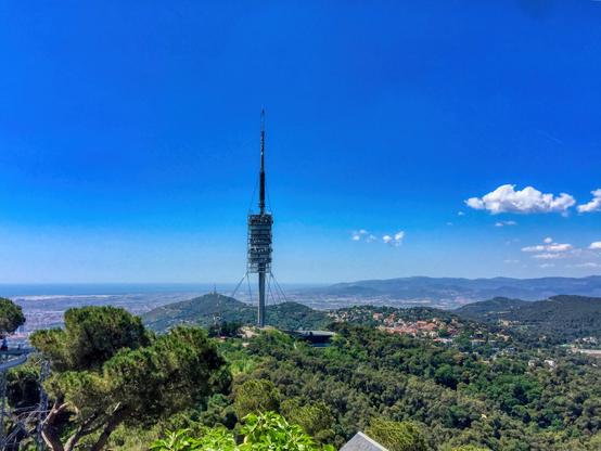 Des d'un punt de mira a Barcelona , Catalunya , hi ha dues figures presents. Sembla que són una parella, probablement d'uns quaranta anys, observant la vista des d'un parc. Al fons, la serra de Collserola i la distintiva Torre de Collserola travessen l'horitzó, mentre que una vegetació exuberant pobla el primer pla, emmarcant la llunyana ciutat.