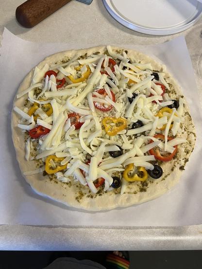 Freshly made pizza topped with sweet peppers, olives and cheese before baking, on a parchment paper