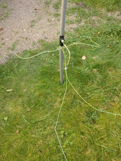 Pied de l'antenne dans la pelouse. Quatre fils partent du connecteur vers le sol, et sont plantés dans la terre tout autour pour assurer une bonne mise à la terre.