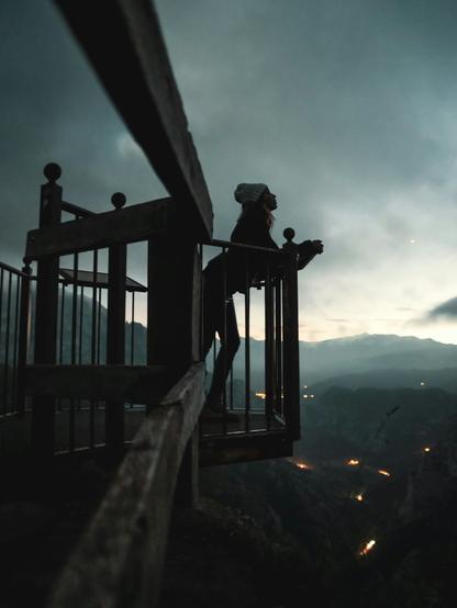 Unsplash photo of a young woman in a white wool cap, leaning on a railing as part of some kind of metal and wood structural viewing platform, high over a valley in the mountains. Late evening skies are darkening, she is mostly silhouetted in shadow, and down below we see a few lights scattered among the dark landscape. Over the mountains the gray clouds are amassing. Mood is mysterious, as in, where is this place? As she looks up at the sky in wonderment. 
Captioned, "a person standing on top of a wooden railing / Cantabria 2021". 

Dated 2021 Dec 14, by Jose P. Ortiz. 
www.Unsplash.com/photos/a-person-standing-on-top-of-a-wooden-railing-bHtn32B9zzc 

www.KronoMoon.org 🏳️‍🌈 ☮️ 
#KronoWatch