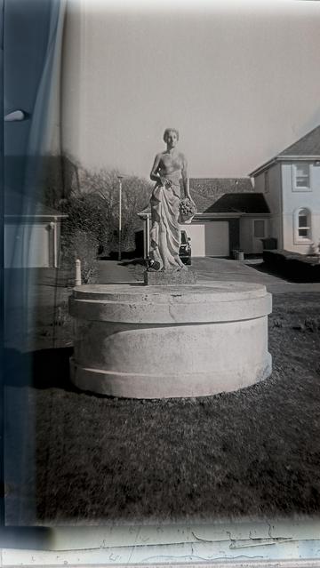 A grainy black and white image of a mock Italian statue in a mock setting. A large blue steak runs down the left hand side of the image.