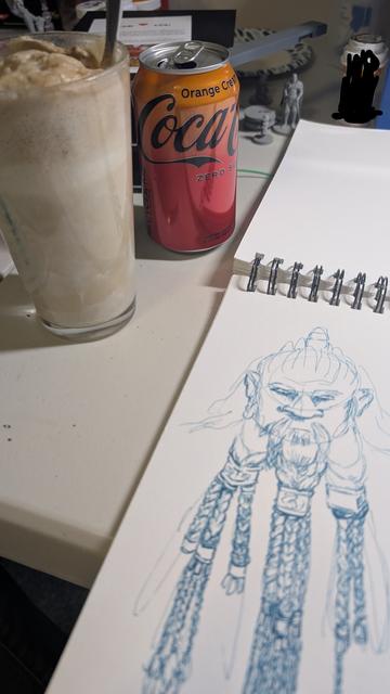 A sketchbook lies in the foreground with a blue pen sketch of a dwarf with an elaborately tri-braided beard. In the background is a pint glass filled with foam and ice cream, and an orange cream Coke zero. There are also other knick-knacks in the background such as D&D figures.