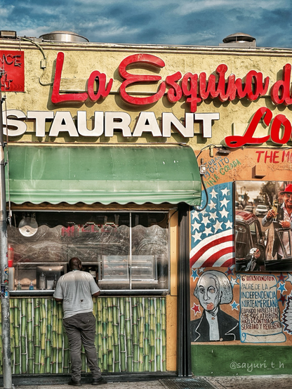 Colorful restaurant sign on the rusted yellow wall. There’s a man at the cafe window ordering next to US flag painting