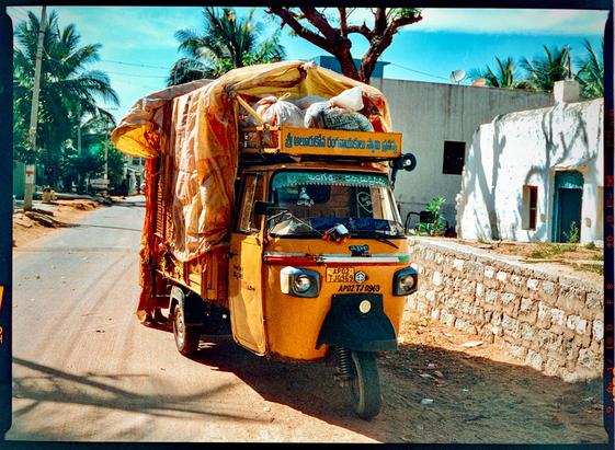 A bright orange auto parked on a dirt road in a rural Indian village.