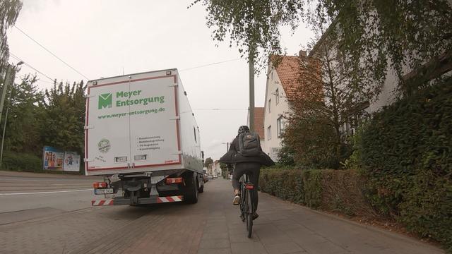 Dashcam-Aufnahme vom Rad aus. Links in einer Parkbucht steht ein LKW, allerdings mit den rechten Reifen aufgesetzt geparkt, sodass der Radverkehr über den Fußweg ausweichen muss.