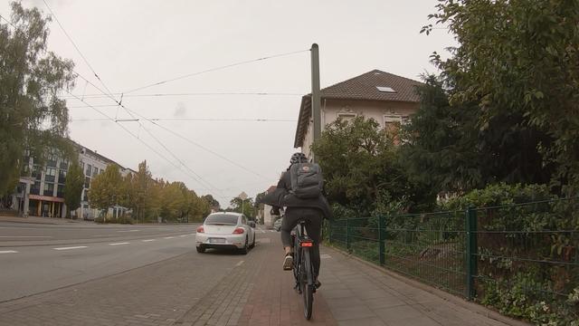 Dashcam-Aufnahme vom Rad aus. links eine Parkbucht, weitgehend leer bis auf ein Auto. Fuß- und Radweg zusammen sind in etwas genauso breit wie die Parkbucht.