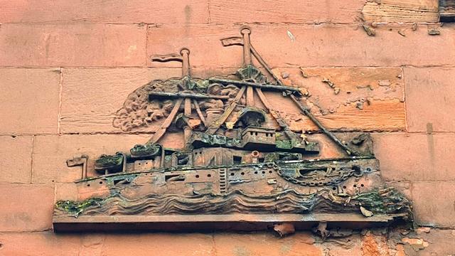 A ship carved onto the facade of a red sandstone tenement building.