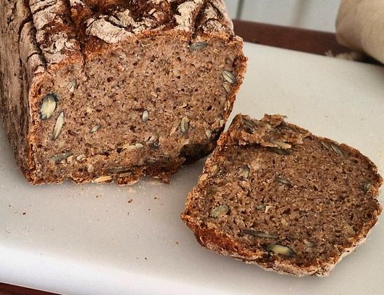 Aufgeschnittenes Vollkornbrot mit Kürbiskernen, Leinsamen und Sonnenblumenkernen.
Auf weisser Schneideplatte.