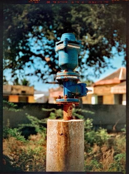 A color photo of a blue painted borewell cap mounted in cement.