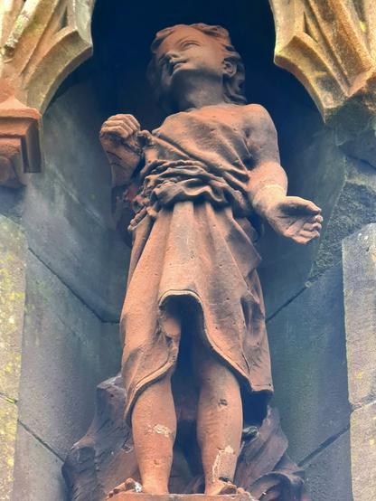 A small statue of jesus as a child wearing a tunic, which has been carved with very realistic folds and creases in it.