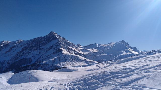 View across a sunny ski track to the peak of the Piz Beverin against a clear blue sky.