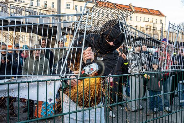 Das Foto von © Björn Obmann zeigt einen Menschen, der mit einer Flex einem Absperrzaun zu Leibe rückt. Im Hintergrund sind zahlreiche Menschen zu sehen, denen das ganz offensichtlich Freude bereitet. Im weiteren Hintergrund sieht man die U-Bahn und eine Häuserzeile
