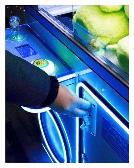 Close up of a hand putting tokens into a claw machine.