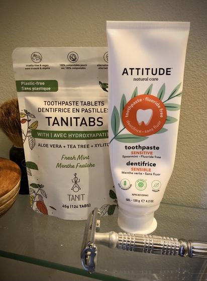 Un paquet de dentifrice en pastilles Tanitabs et un tube de dentifrice Attitude, le tout sur une tablette de salle de bain.