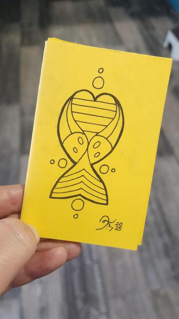 Mini zine by Danilynn Jiibay. Front cover depicting a pride heart, two spirit feathers, a design reminiscent of the progress emblem, and circles representing all directions. Unintentionally, it looks like a fish.