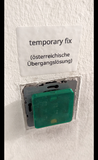 a broken open stairway light switch, temporarily improved with a 3D printed cover.

Above the switch, there is a sticker which reads: "temporary fix (österreichische Übergangslösung)"