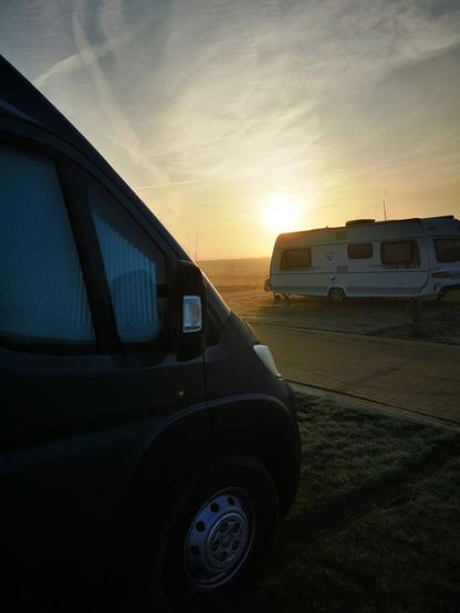 Wohnmobil und Wohnwagen auf einem Campingplatz. Die Sonne geht auf, die Wiese ist noch gefroren