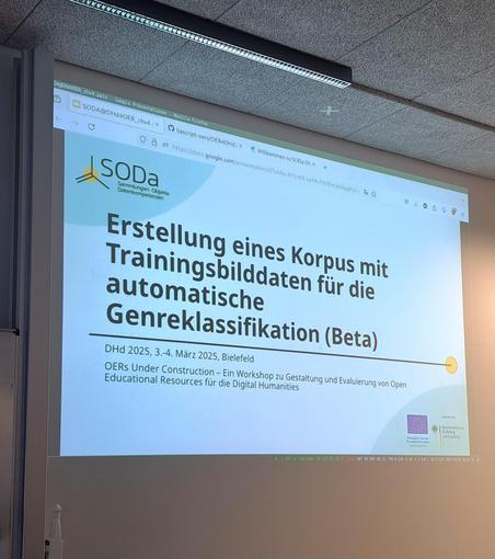 Das Bild zeigt eine Projektion auf eine Leinwand. Auf der Leinwand ist eine Präsentationsfolie zu sehen mit dem Titel: "Erstellung eines Korpus mit Trainingsbilddaten für die automatische Genreklassifikation (Beta)". Darunter stehen Informationen zum Datum und Ort: "DHd 2025, 3.-4. März 2025, Bielefeld". Weiter unten wird ein Workshop beworben: "OERs Under Construction - Ein Workshop zu Gestaltung und Evaluierung von Open Educational Resources für die Digital Humanities". Das Logo von SODA ist oben links platziert. Unten rechts sind die Logos der Europäischen Union und des Bundesministeriums für Bildung und Forschung zu sehen. Oben auf der Leinwand ist der obere Rand eines Computerbildschirms sichtbar, der die Präsentation geöffnet hat.