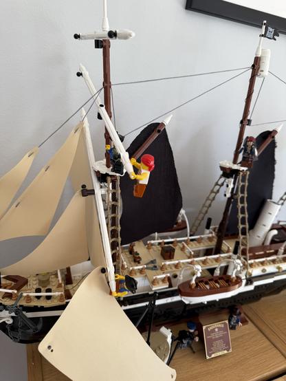 A detailed model of a sailing ship is displayed, featuring multiple sails and rigging. Several mini-figures are depicted climbing the masts and adjusting the sails. The ship's nameplate reads "Endurance," and it rests on a wooden surface
