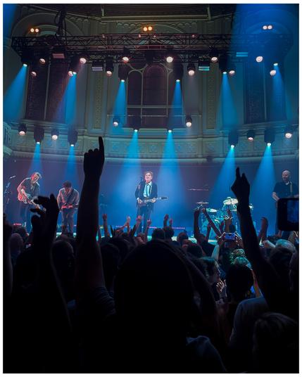 A rock band performing, with the public dancing and waving hands