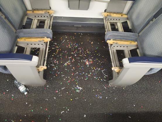 Sol d'un train jonché de confettis dans un carré. Les assises des sièges sont démontées mais ça c'est pas fait par les clients.