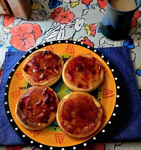 Four thick pancakes topped with Lingonberry jam and a little pure maple syrup, on a Laurel Burch plate. In background: floral tablecloth, pepper shaker, napkin holder, and a ceramic mug (made by an old friend) with extra creamy coffee.