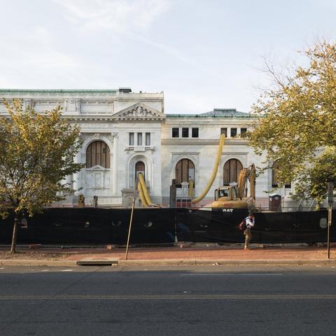 Man walking on the sidewalk in front of a library under renovation with construction equipment outside