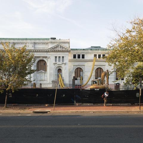 Man walking on the sidewalk in front of a library under renovation with construction equipment outside