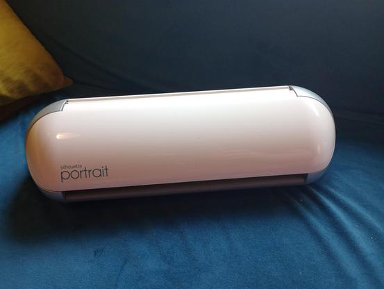 a white electronic device with a paper slot, labeled "Silhouette Portrait"