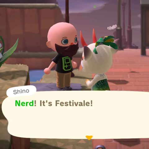 Animal Crossing: New Horizons screenshot. Image is set along the edge of the town square with Shino (white deer with long red horns) seen from behind wearing a green dress and a headpiece for Festivale talking to a light skinned, thick bearded, bald human villager wearing a black t-shirt with a Gameboy outline on it. Shino is saying, "Nerd! It's Festivale!"