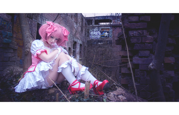 Cosplayer als Madoka Kaname sitzt inmitten eines zerstörten Gebäudes. Sie leuchtet leicht inmitten der kargen Umgebung.