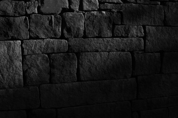 black and white photograph of a stone wall of bricks of various sizes partly lit by bright sunshine