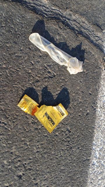 Used magnum sized condom with Magnum wrapper discarded on the pavement