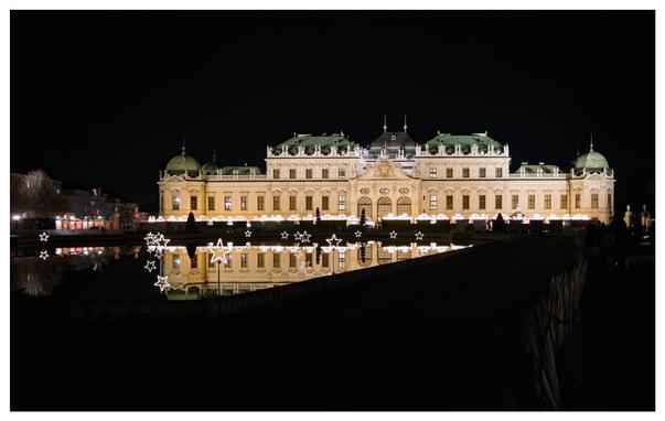 The Belvedere Palace in Vienna, Austria, beautifully lit up at night, with its reflection shimmering in the water below.