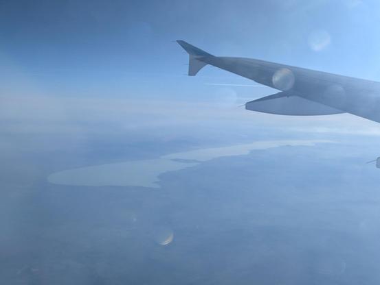 The wing of the plane on the right side. The lake in the center. There is a bit of fog but no clouds.