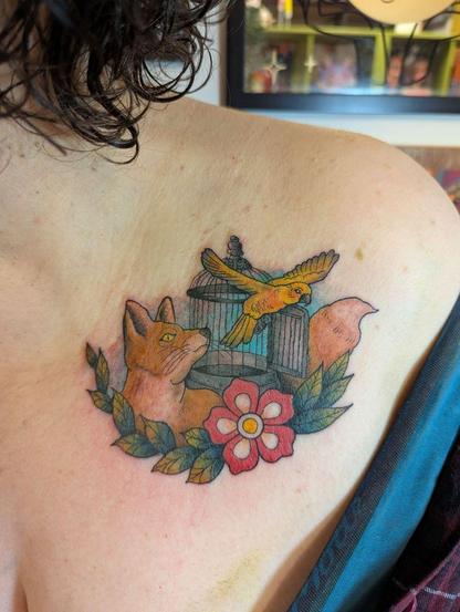 A woman's shoulder with a colourful tattoo of a fox watching a bird fly from a cage