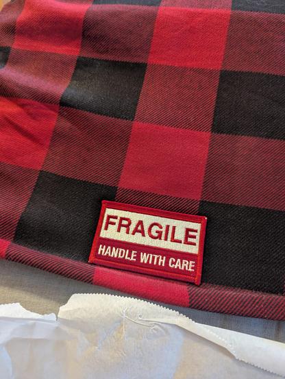 A "Fragile Handle with Care" shipping label as a patch, placed at the bottom back center of a buffalo check coat.