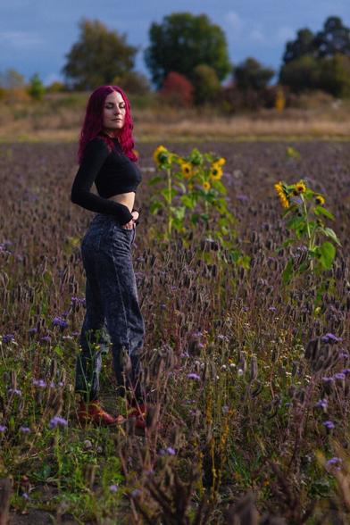 A woman wearing jeans and crop top in the middle of field of flowers in autumn with her eyes closed