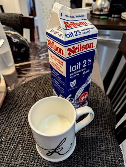 A milk carton with French labels and a mug half full of 2% skimmed milk. The milk brand is 100% Canadian.