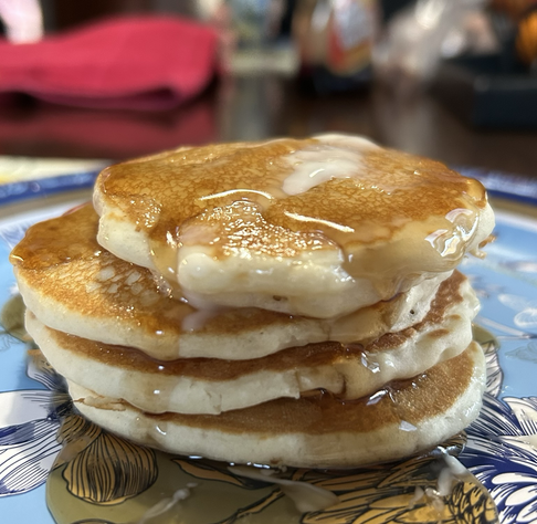 A stack of four small golden brown pancakes with butter and syrup  on a blue and white floral plate.